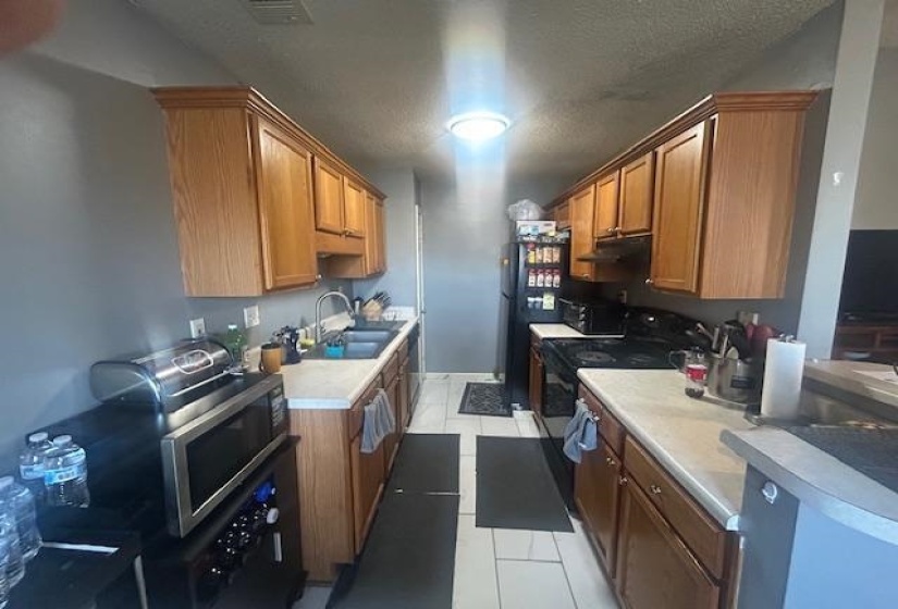 Kitchen featuring black range with electric stovetop, light tile patterned flooring, brown cabinets, light countertops, and stainless steel microwave