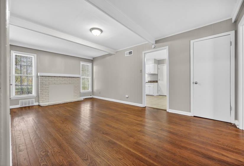 Unfurnished living room featuring beam ceiling, dark wood-type flooring, ornamental molding, a brick fireplace, and wooden walls
