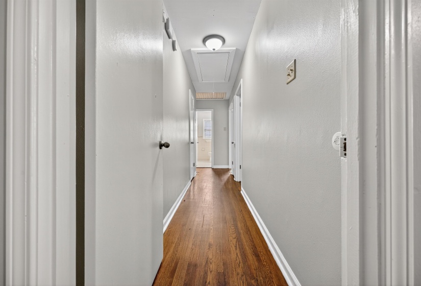 Hallway featuring attic access, dark wood-type flooring, and a textured wall