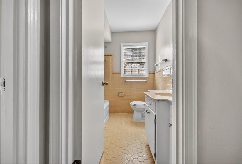 Bathroom with tile walls, light tile patterned floors, vanity, wainscoting, and a tub to relax in