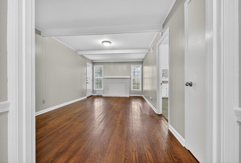Unfurnished living room featuring dark wood-type flooring, beam ceiling, ornamental molding, and wooden walls