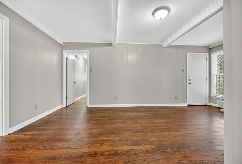 Unfurnished living room featuring beamed ceiling, dark wood finished floors, crown molding, and wood walls