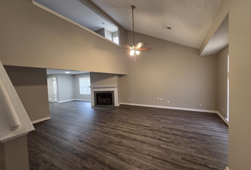 Unfurnished living room featuring dark wood-style flooring, a ceiling fan, a tile fireplace, and high vaulted ceiling