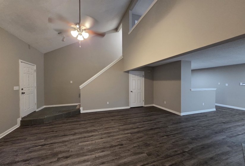 Unfurnished living room featuring dark wood-type flooring, high vaulted ceiling, and ceiling fan