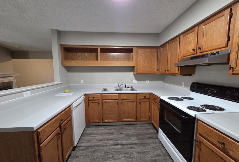 Kitchen featuring electric range oven, open shelves, a textured ceiling, light countertops, and under cabinet range hood