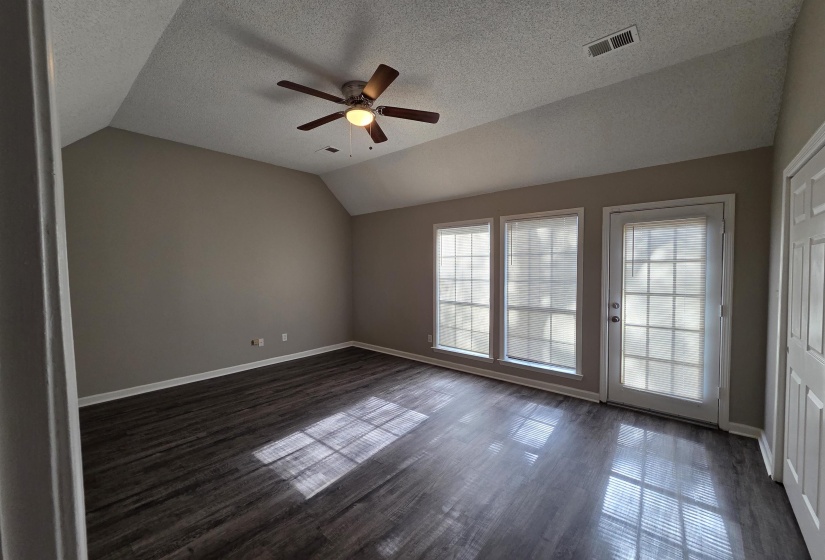 Empty room with vaulted ceiling, a textured ceiling, dark wood-type flooring, and a ceiling fan