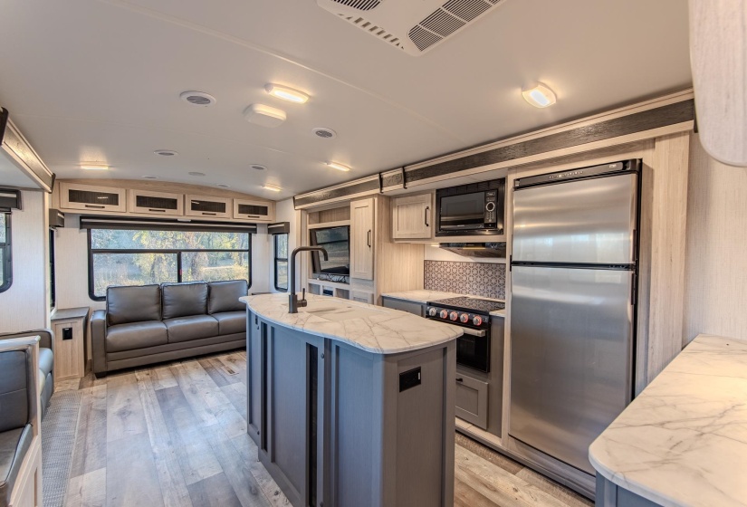 Kitchen with an island with sink, light wood-style floors, light stone countertops, black appliances, and open floor plan