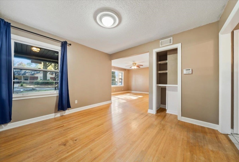 Empty room with a textured ceiling, light wood-style flooring, ceiling fan, and built in shelves