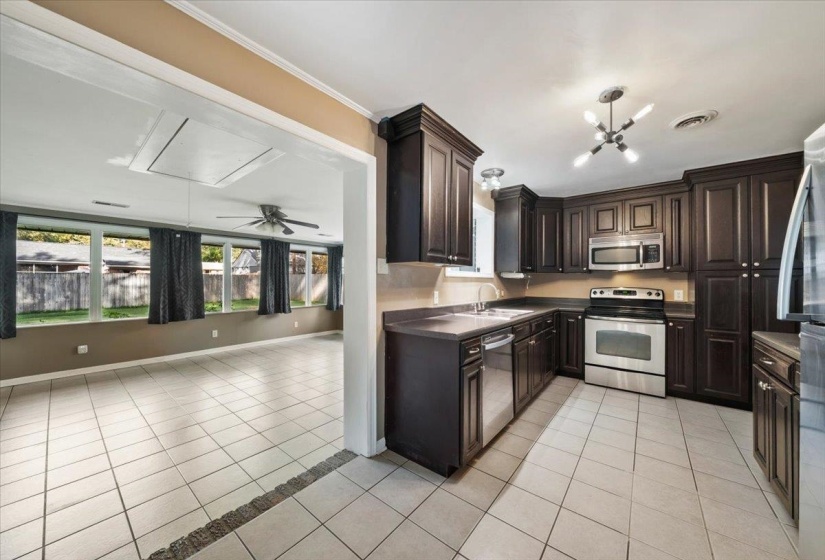 Kitchen with light tile patterned floors, dark brown cabinets, appliances with stainless steel finishes, ceiling fan, and crown molding