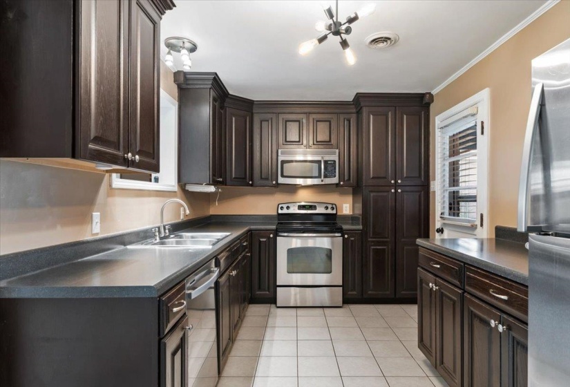 Kitchen with dark countertops, dark brown cabinets, appliances with stainless steel finishes, light tile patterned floors, and crown molding
