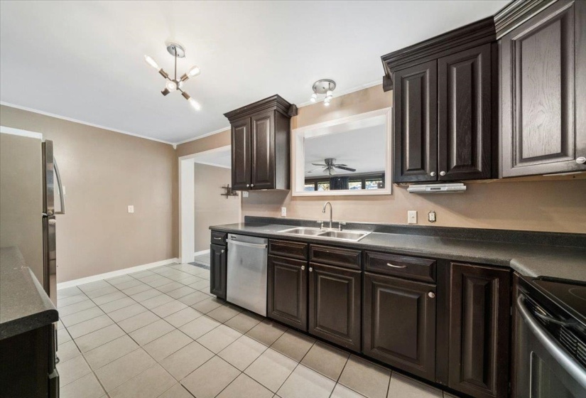 Kitchen with dark brown cabinetry, dark countertops, appliances with stainless steel finishes, light tile patterned flooring, and crown molding