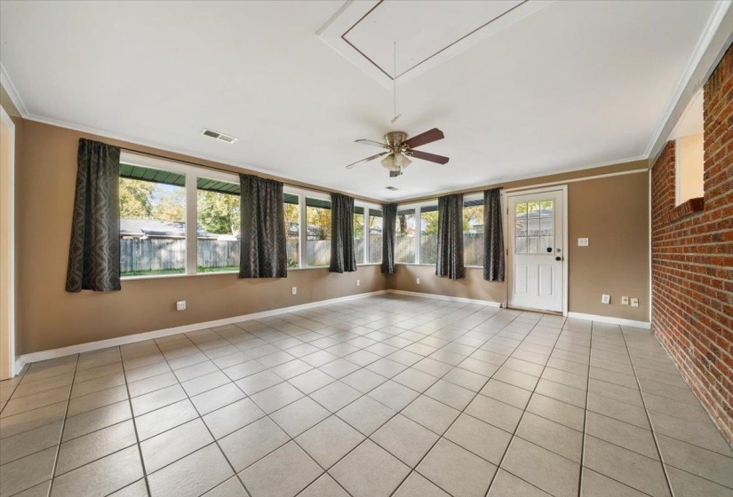 Empty room featuring brick wall, crown molding, light tile patterned flooring, attic access, and ceiling fan