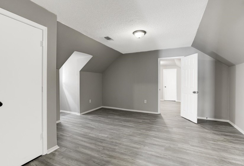 Bonus room with light wood-style flooring, a textured ceiling, and vaulted ceiling
