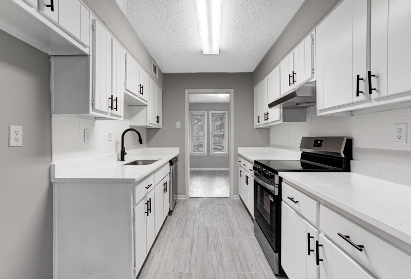 Kitchen featuring appliances with stainless steel finishes, tasteful backsplash, a textured ceiling, under cabinet range hood, and light stone countertops