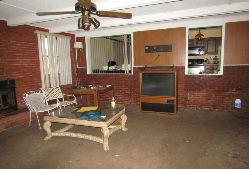 Living area with brick wall, a wood stove, and ceiling fan