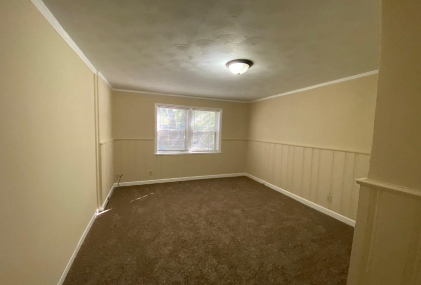 Unfurnished room featuring dark carpet, crown molding, and a wainscoted wall