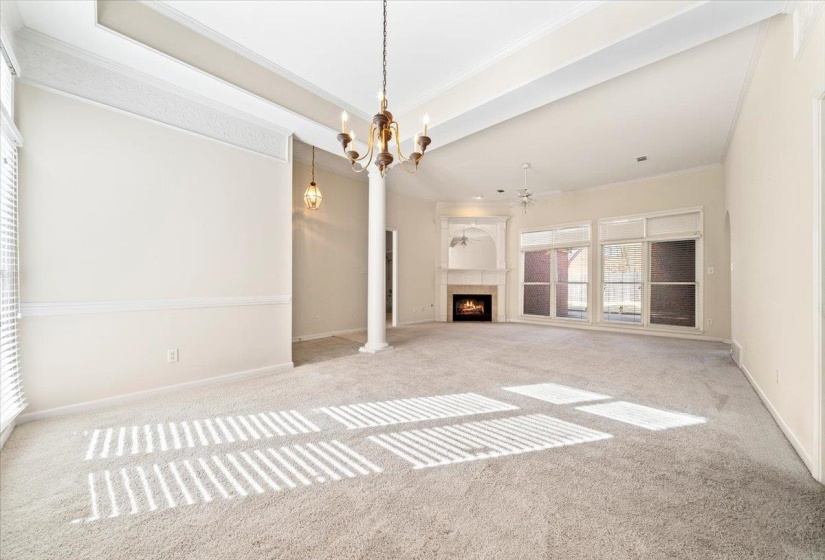 Unfurnished living room with ornamental molding, carpet, a chandelier, a lit fireplace, and a ceiling fan
