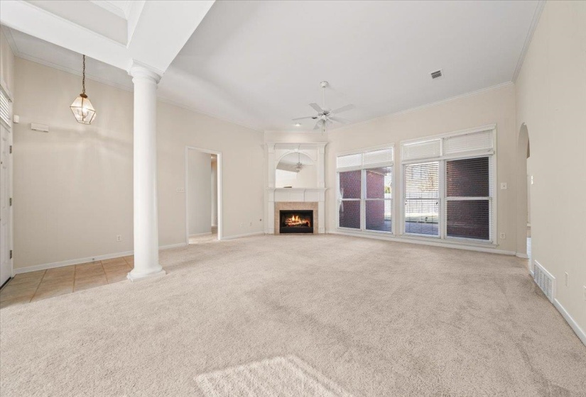 Unfurnished living room featuring a tiled fireplace, light carpet, decorative columns, ornamental molding, and a ceiling fan