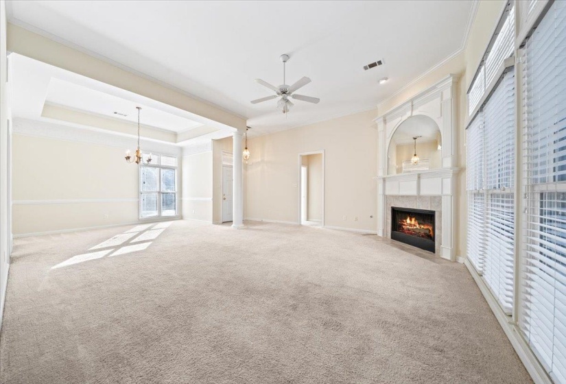 Unfurnished living room with ornamental molding, a tiled fireplace, carpet, a raised ceiling, and ceiling fan