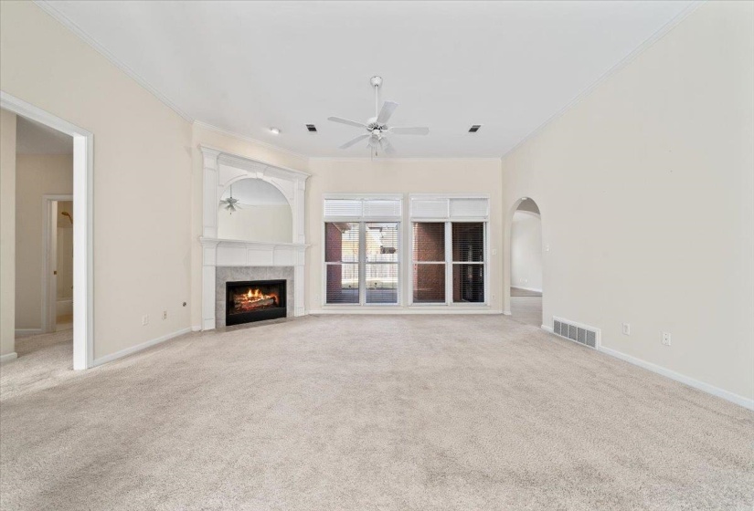Unfurnished living room featuring crown molding, a tile fireplace, light carpet, arched walkways, and a ceiling fan