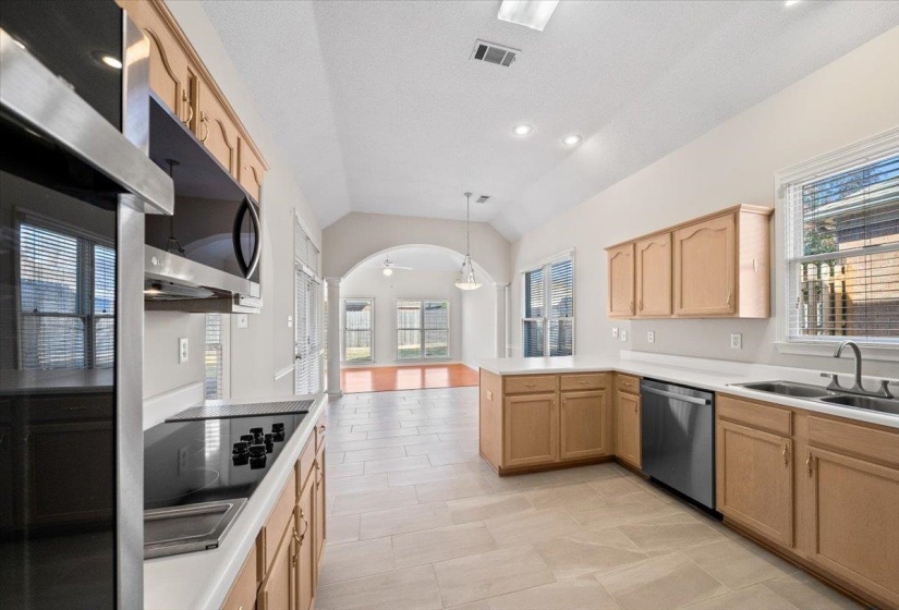 Kitchen featuring vaulted ceiling, light brown cabinetry, light countertops, decorative light fixtures, and stainless steel dishwasher