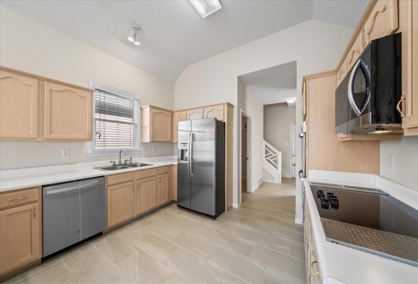 Kitchen with light brown cabinets, stainless steel appliances, vaulted ceiling, and light countertops