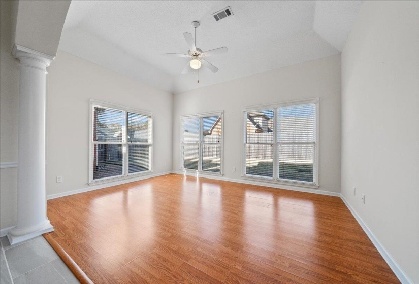 Unfurnished living room featuring ornate columns, light wood-style flooring, ceiling fan, vaulted ceiling, and a textured ceiling