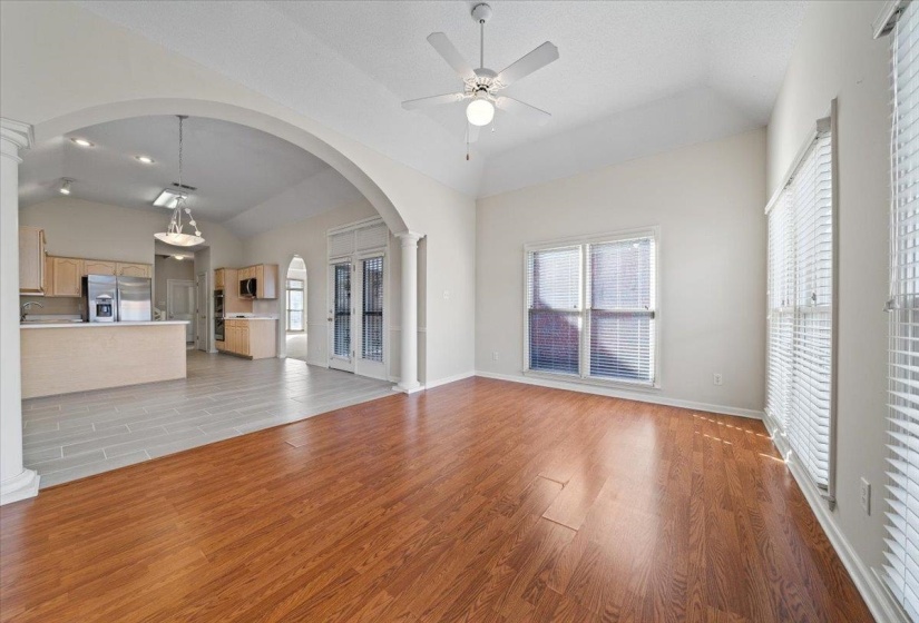 Unfurnished living room with light wood finished floors, arched walkways, lofted ceiling, ceiling fan, and decorative columns