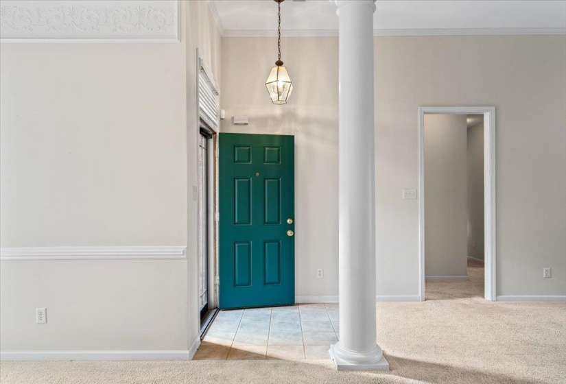 Carpeted entrance foyer featuring tile patterned flooring, ornamental molding, and ornate columns