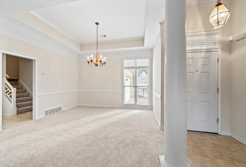 Foyer with a raised ceiling, ornamental molding, a chandelier, light carpet, and light tile patterned floors