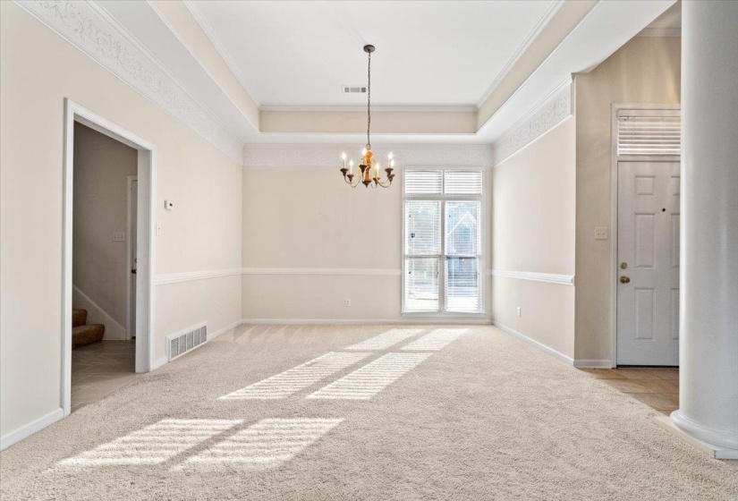 Unfurnished room with a tray ceiling, light carpet, crown molding, a chandelier, and stairway