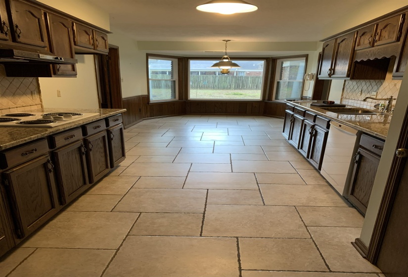 Kitchen featuring decorative backsplash, dark brown cabinetry, dark stone counters, a wainscoted wall, and wood walls