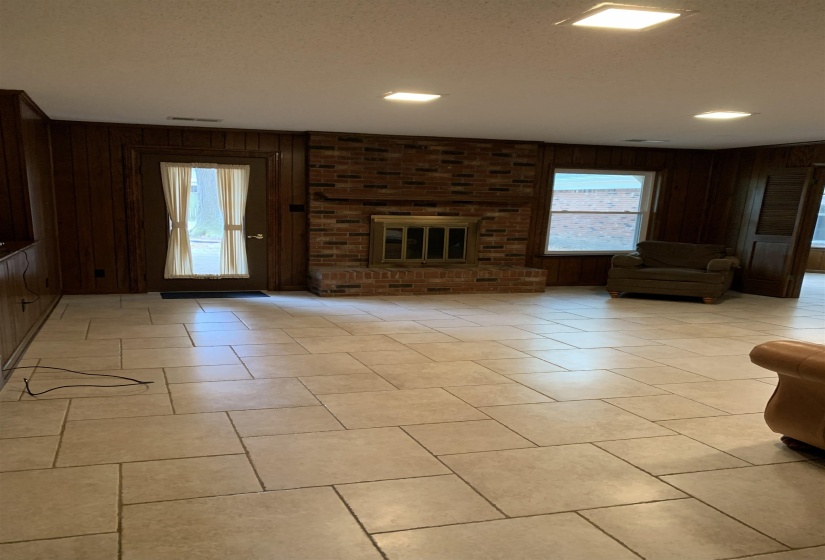 Unfurnished living room featuring wood walls, plenty of natural light, a brick fireplace, a textured ceiling, and light tile patterned floors