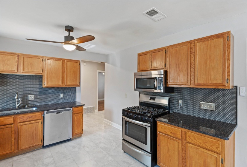 Kitchen with tasteful backsplash, stainless steel appliances, ceiling fan, and dark stone countertops