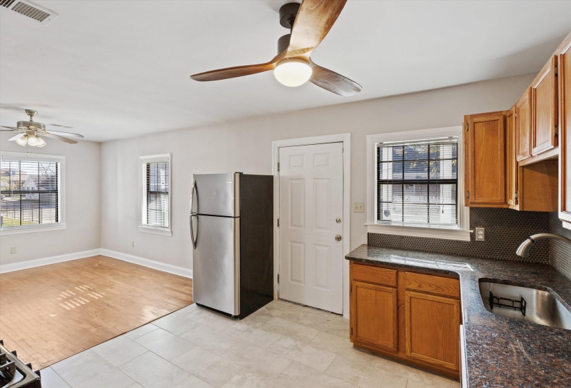 Kitchen with dark stone countertops, freestanding refrigerator, brown cabinets, and a ceiling fan