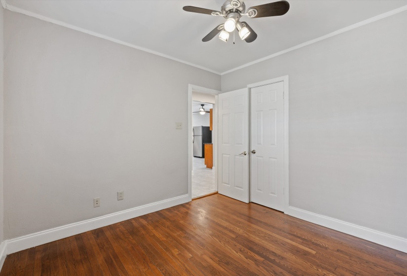 Unfurnished bedroom featuring wood finished floors, ornamental molding, freestanding refrigerator, a ceiling fan, and a closet