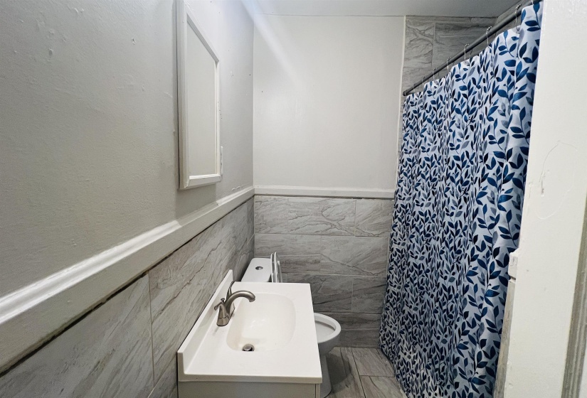 Full bathroom featuring tile walls, curtained shower, wainscoting, and vanity