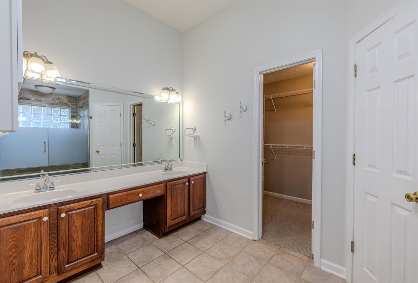 Primary bathroom featuring double vanity, light tile flooring, a spacious closet, and a shower stall