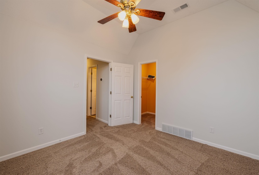 Unfurnished bedroom with carpet, a spacious closet, ceiling fan, and high vaulted ceiling