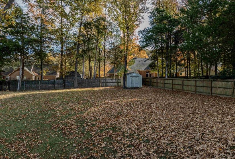 Fenced backyard featuring a storage unit and view of scattered trees
