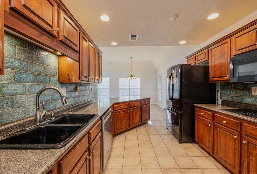 Kitchen with decorative backsplash, a peninsula, brown cabinets, black appliances, and light tile patterned flooring