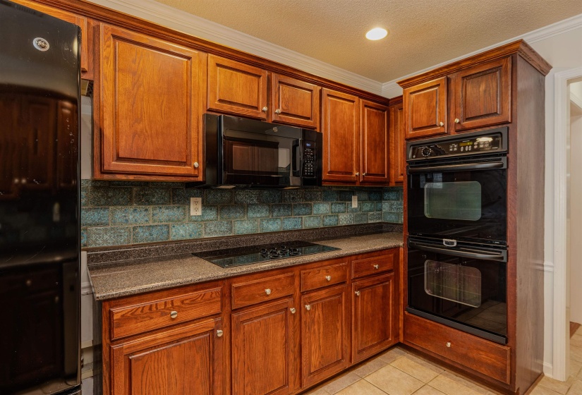 Kitchen featuring black appliances, ornamental molding, light tile patterned floors, tasteful backsplash, and brown cabinets