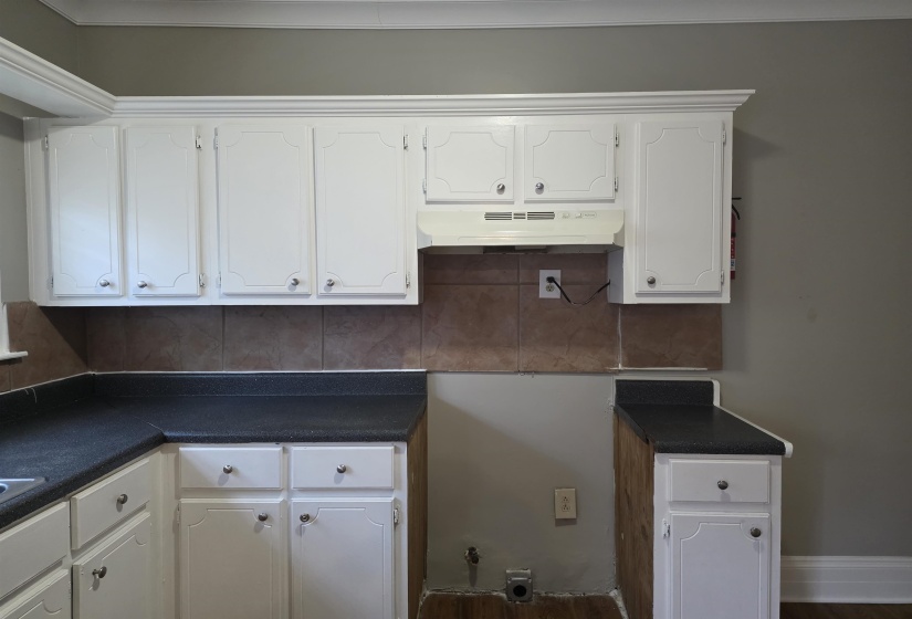 Kitchen with white cabinetry, dark countertops, and under cabinet range hood