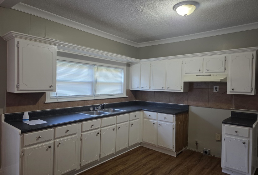 Kitchen featuring dark countertops, white cabinets, dark wood-style flooring, a textured ceiling, and ornamental molding