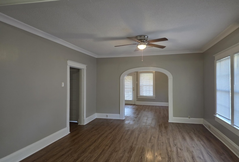 Unfurnished room featuring dark wood-style flooring, crown molding, arched walkways, healthy amount of natural light, and a textured ceiling