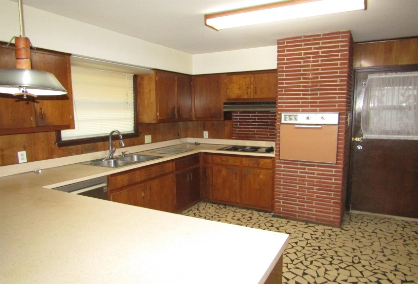 Kitchen with light countertops, pendant lighting, brown cabinetry, ventilation hood, and electric cooktop