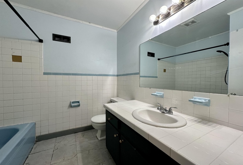 Bathroom with crown molding, vanity, tile walls, light marble finish flooring, and washtub / shower combination