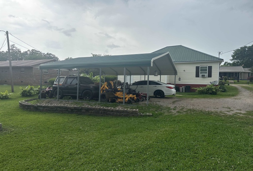 Rear view of house with a lawn, dirt driveway, a metal roof, and a detached carport