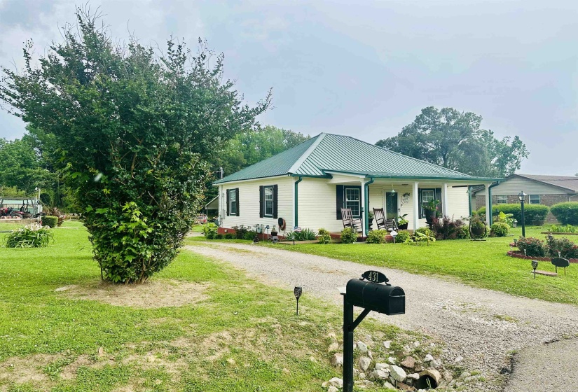 View of front of house with covered porch, a front yard, a metal roof, and driveway