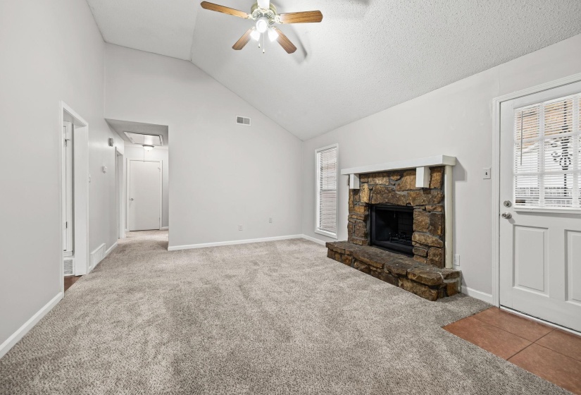 Unfurnished living room featuring carpet, high vaulted ceiling, attic access, a ceiling fan, and a fireplace